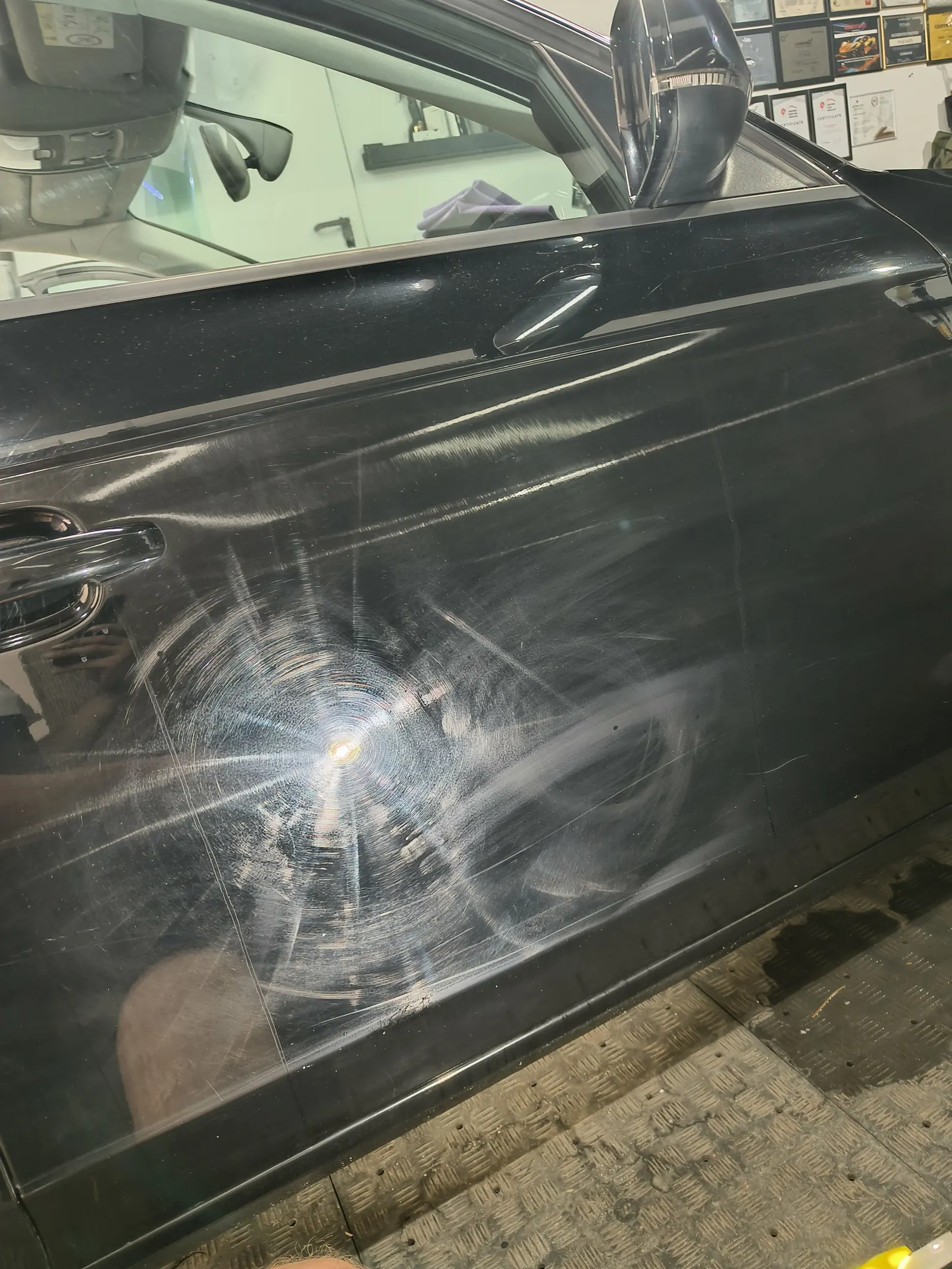 Okrągłe rysy i hologramy na czarnym lakierze drzwi przed korektą