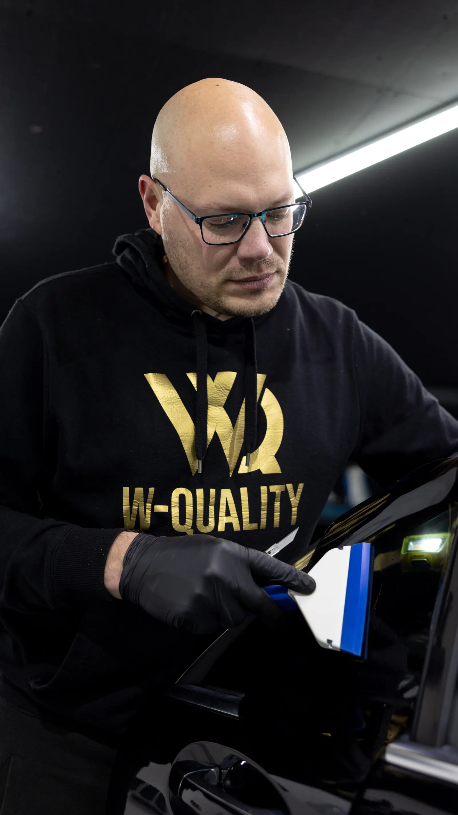 Bartosz Wróblewski przyciemnia szybę w drzwiach czarnego auta w studiu W-Quality